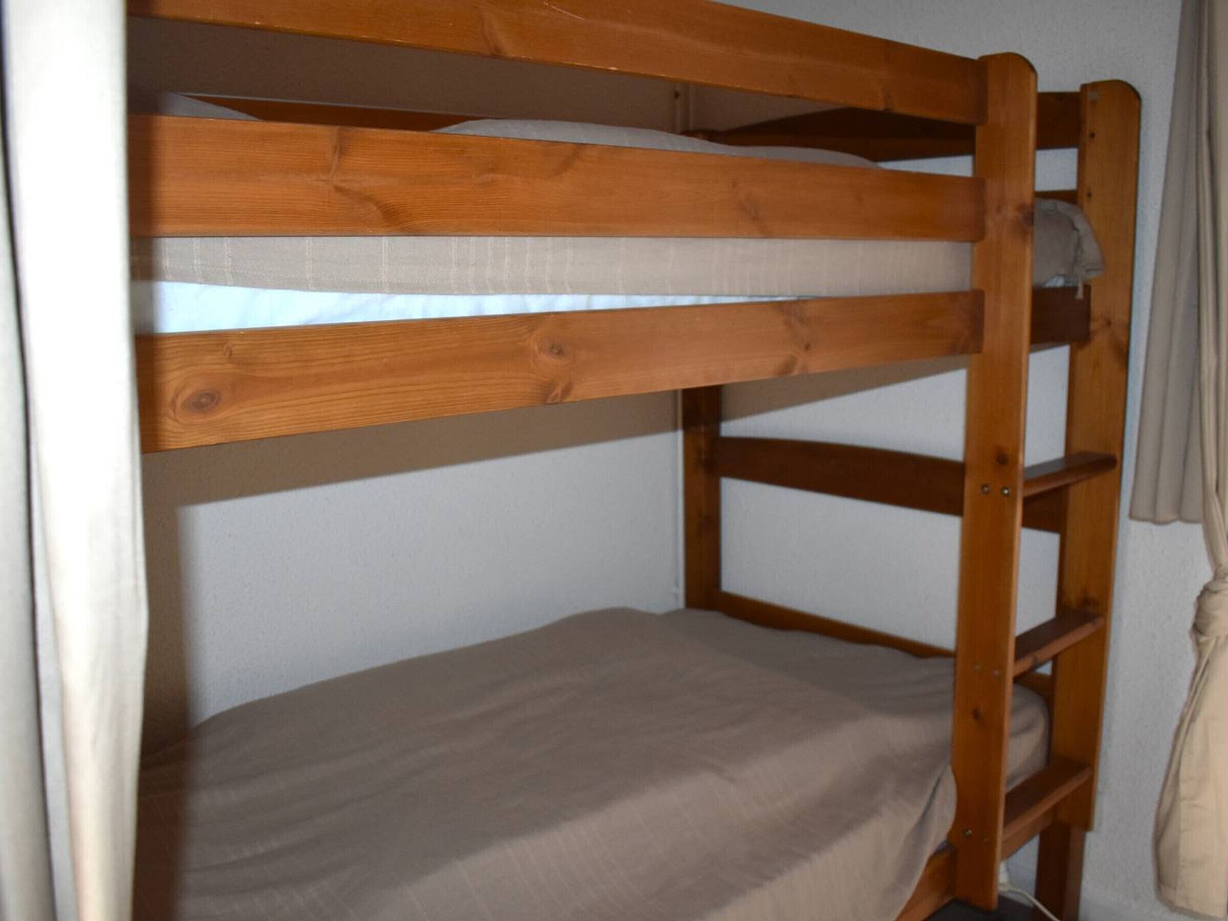 A bunk bed with wooden frames and a beige mattress.