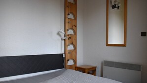 Un dormitorio con cama, cabecero de madera, mesita de noche pequeña de madera, espejo y radiador.