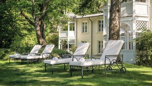 Outdoor lounge chairs arranged in a row on a grassy lawn, with a large building in the background. - Double room Comfort - ROEWERS Privathotel & Spa (Sellin)