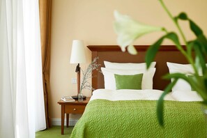 Ein Hotelzimmer mit einem ordentlich bezogenen Bett, einem Nachttisch mit Lampe und einer Blumenvase, sowie einem grünen Teppich.