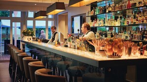 Eine Bar mit einer langen Theke, mehreren Hockern sowie einer Auswahl an Flaschen und Gläsern.