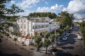 Ein historisches Gebäude mit Innenhof, mehreren Balkonen und Blick auf die Straße mit parkenden Autos und Bäumen.