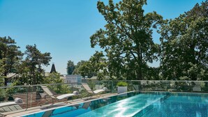 Ein klares, blaues Schwimmbecken mit Liegestühlen und Blick auf Bäume sowie Gebäude im Hintergrund.