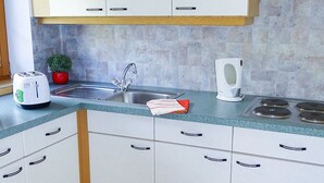 Una cocina moderna con armarios blancos, un lavamanos de acero inoxidable, un tostador y una tetera.