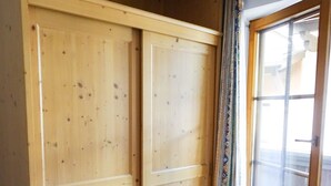 Una habitación con un armario de madera, una puerta corrediza de vidrio y piso de baldosas.