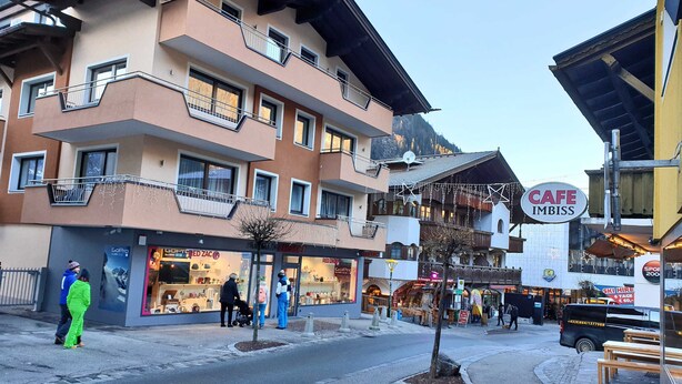 Un edificio de varios pisos con balcones, un letrero de cafetería y diversas tiendas.