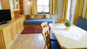 Una habitación pequeña con cama, una mesa de comedor, sillas, un televisor y una ventana con cortinas.