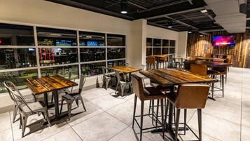 A modern restaurant with high tables and chairs, large windows, and a TV on the wall.