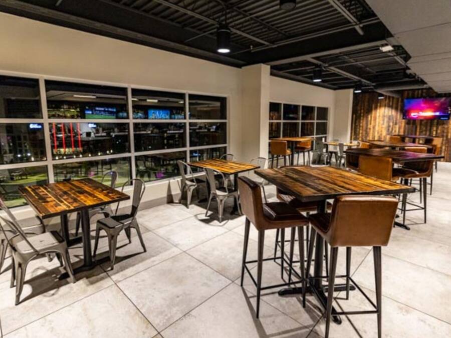 A modern restaurant with high tables and chairs, large windows, and a TV on the wall.
