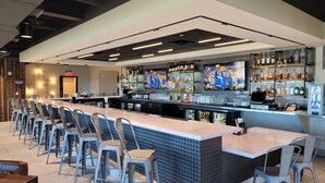A modern bar area with a long counter, bar stools, and a variety of liquor bottles. - Homewood Suites by Hilton Tuscaloosa Downtown (Tuscaloosa)