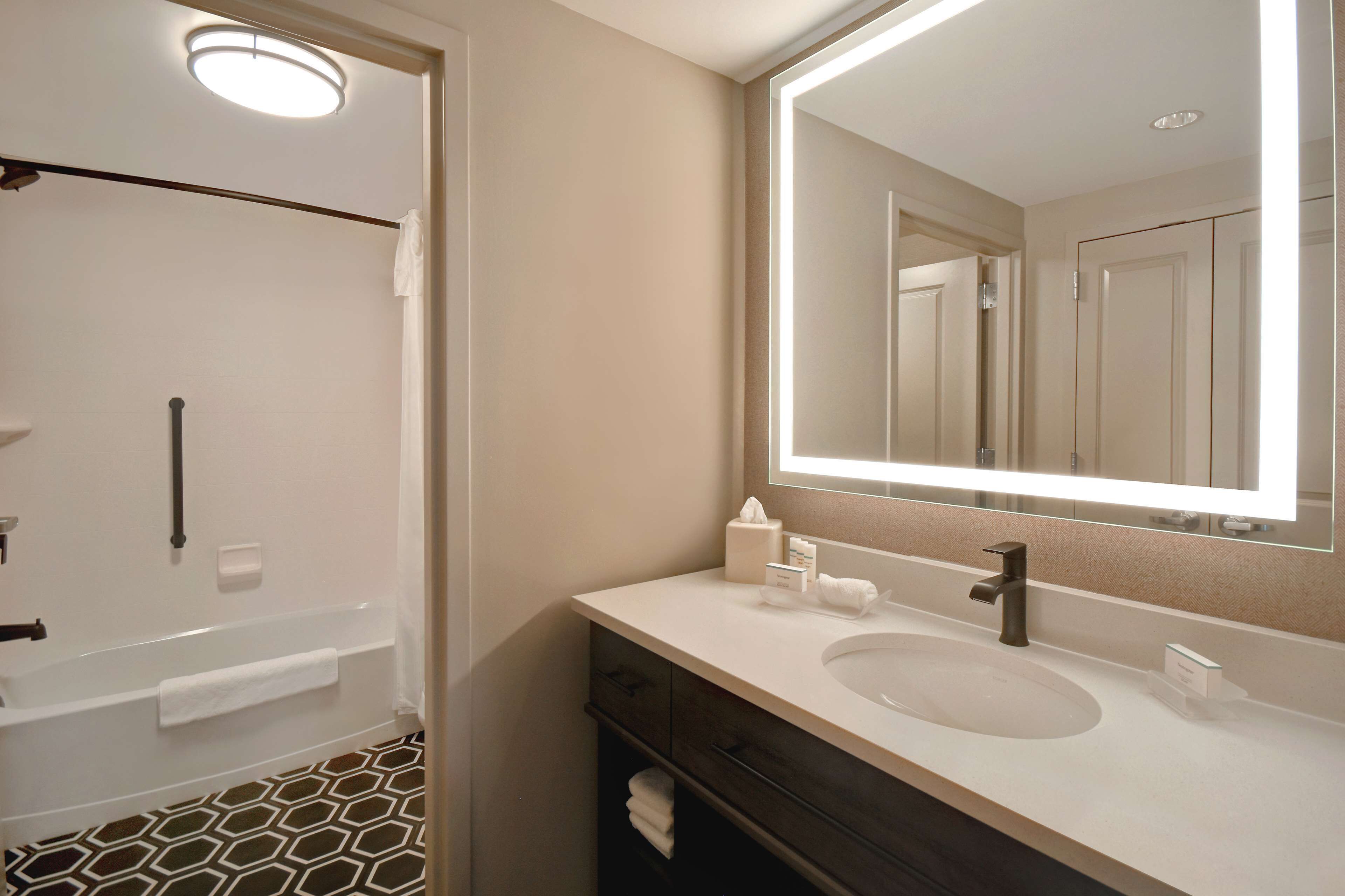 A bathroom with a white sink, dark vanity, and a large mirror.