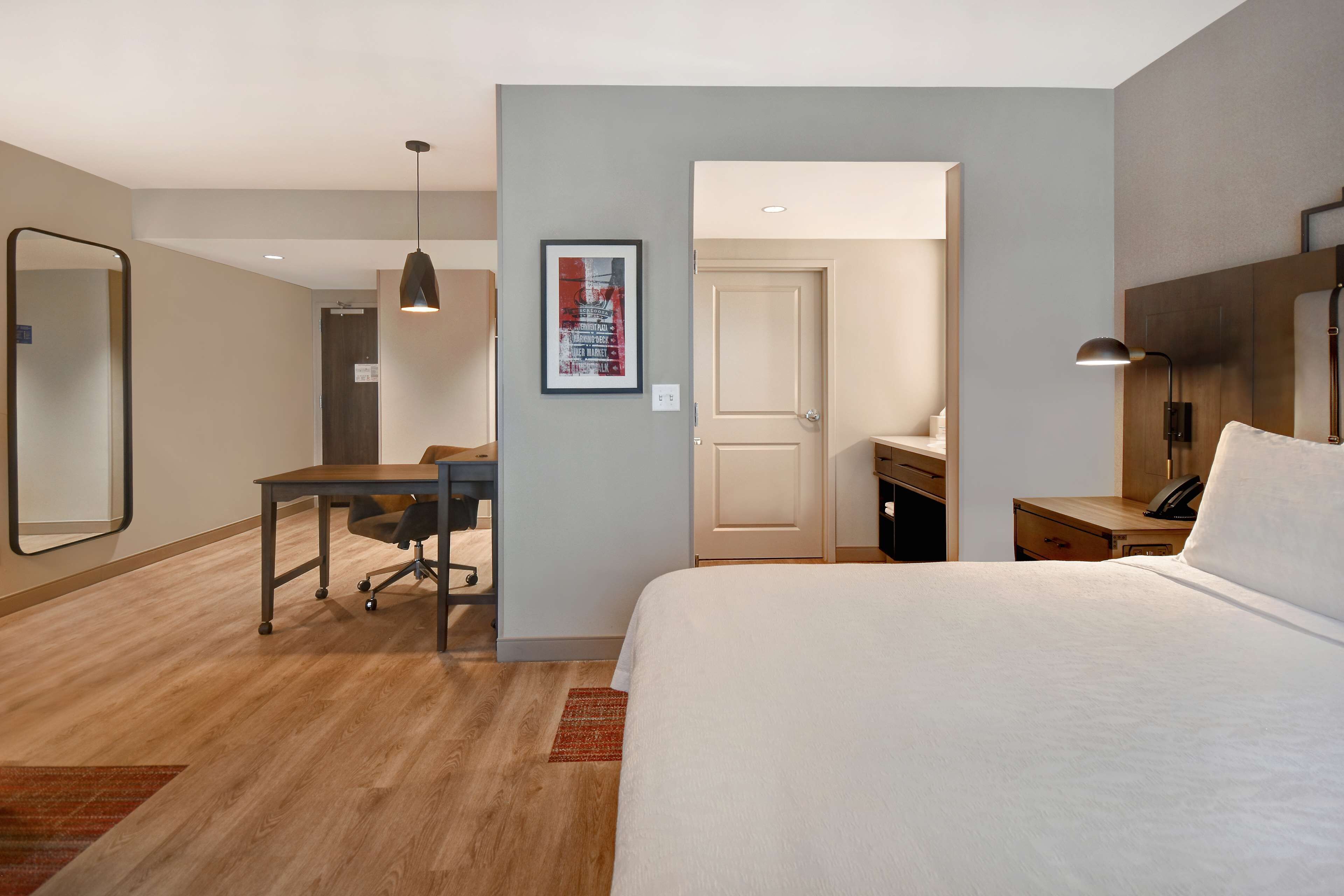 Una habitación de hotel con cama, escritorio, silla y espejo.