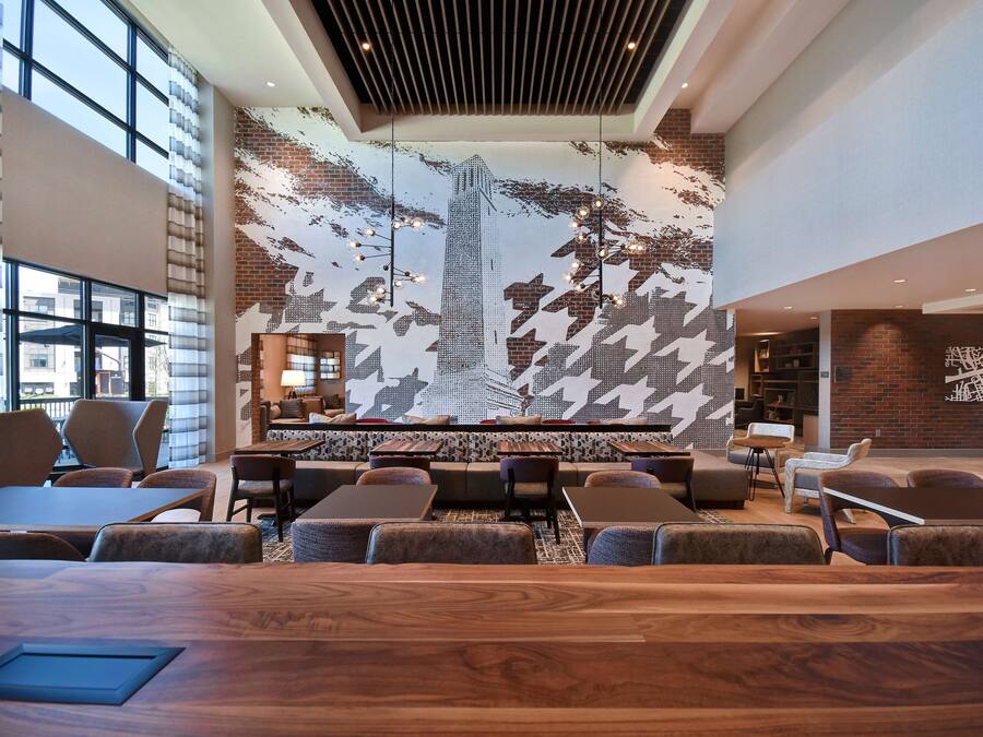 Un área de estar moderna con un mural grande de un paisaje urbano, asientos cómodos y un mostrador de recepción de madera.