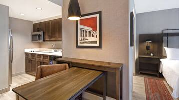 Una habitación de hotel moderna con una mesa de comedor de madera, una zona de cocina con microondas y una cama con mesita de noche.