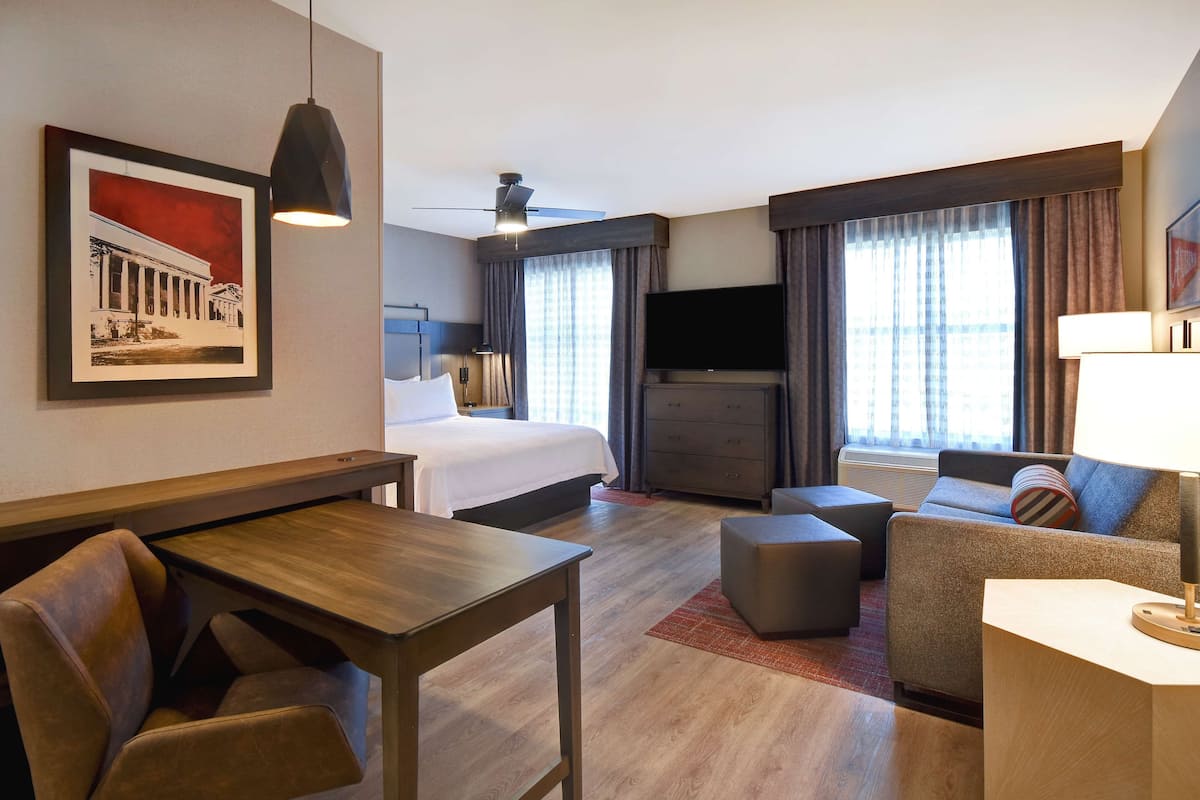 A hotel room with a bed, a desk, a sofa, a TV, and a ceiling fan.