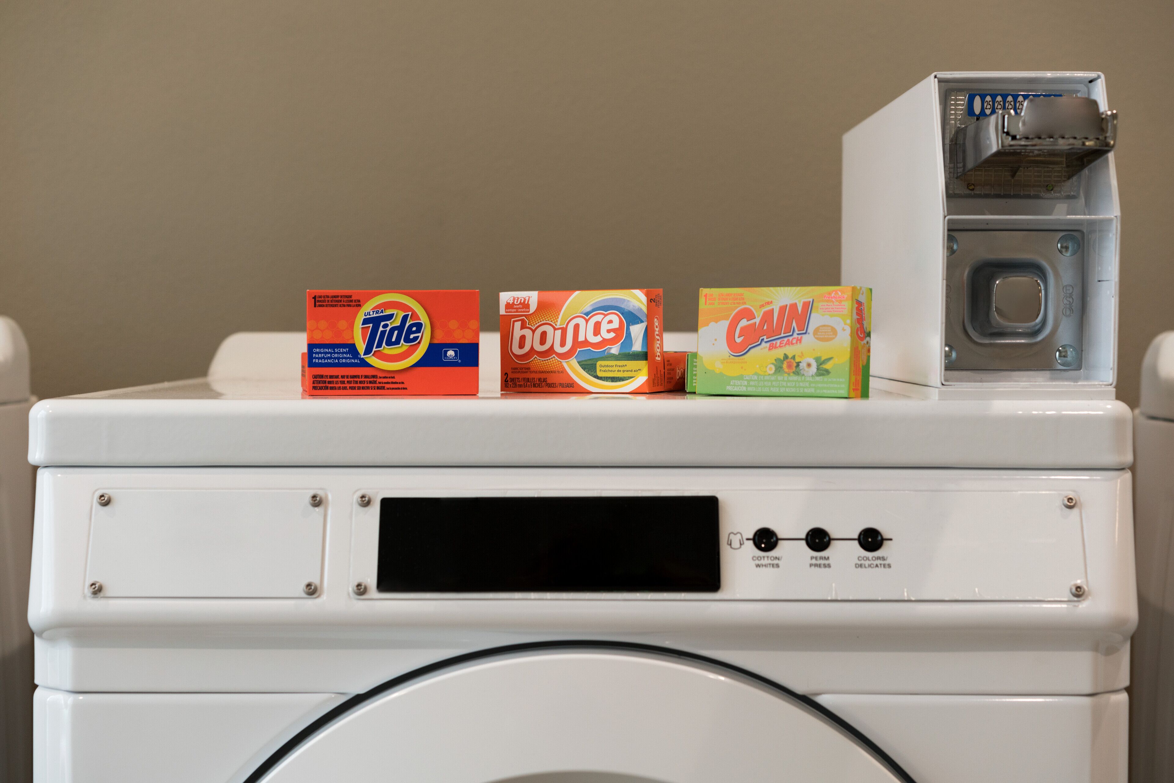 A front-loading washing machine with Tide, Bounce, and Gain detergent boxes on top.