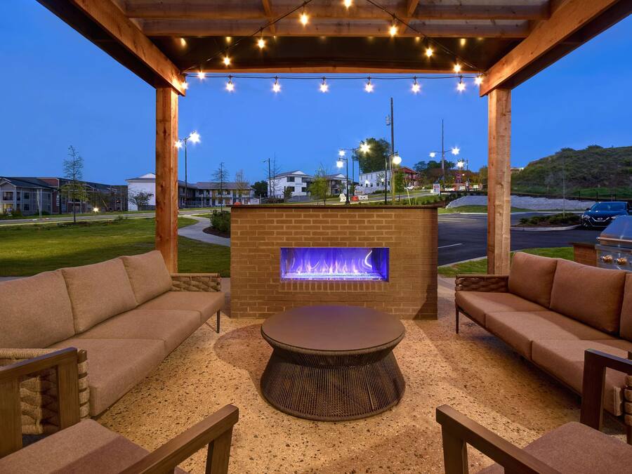 An outdoor patio with a brick fireplace, seating, and string lights.