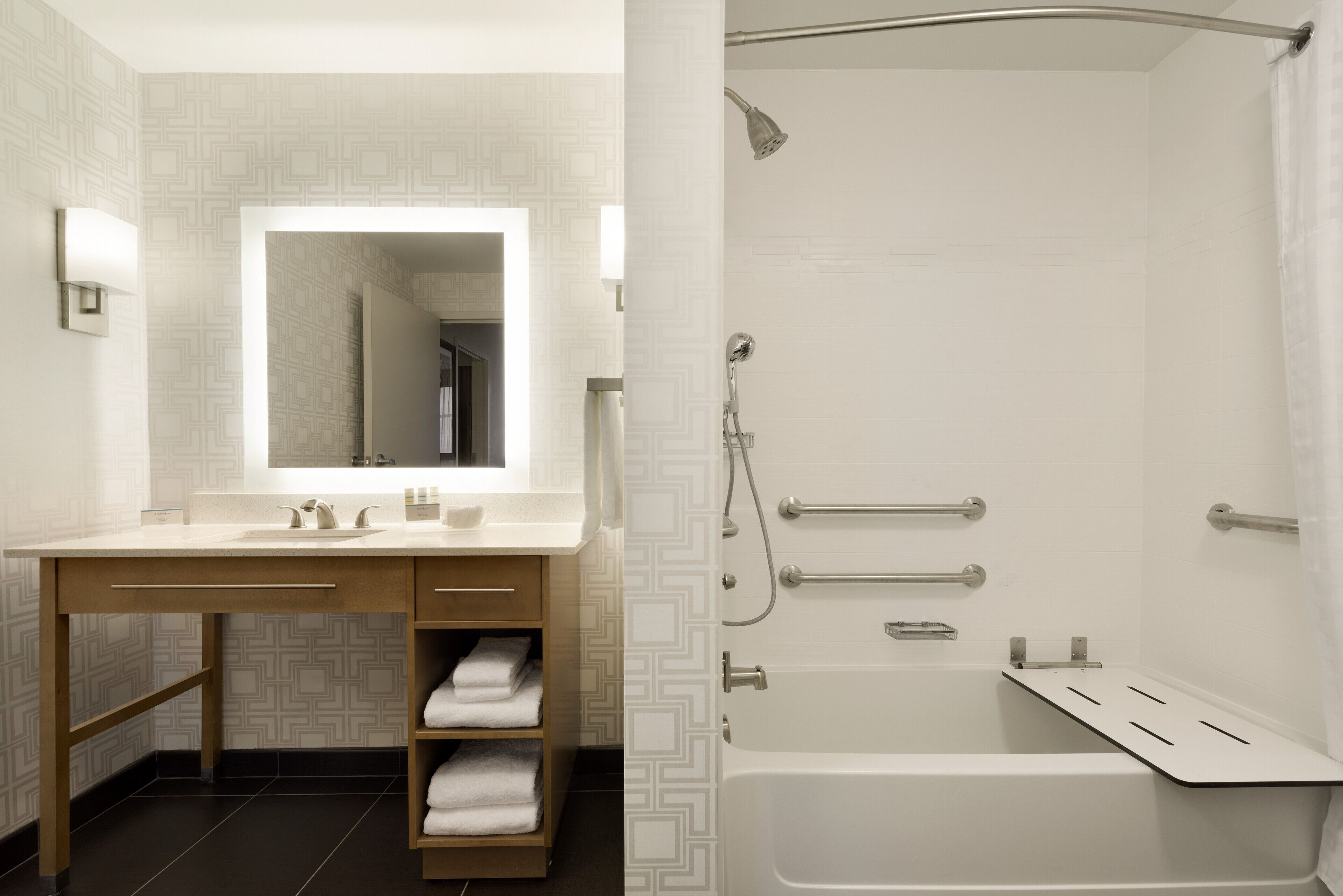 A modern bathroom with a large mirror, a bathtub, and a shower with grab bars.