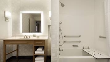 A modern bathroom with a large mirror, a bathtub, and a shower with grab bars.