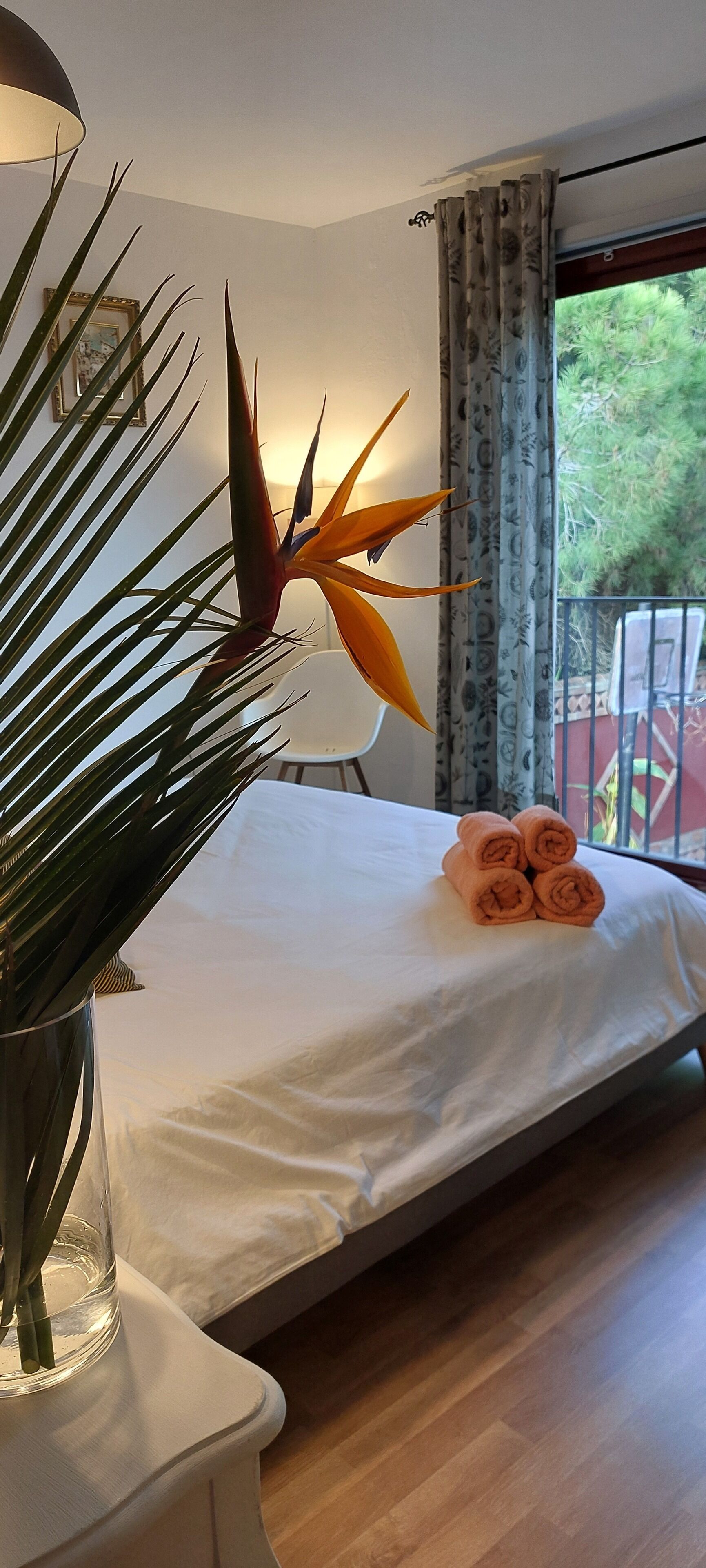 A bedroom with a bed, a potted plant, a lamp, and a window with curtains.