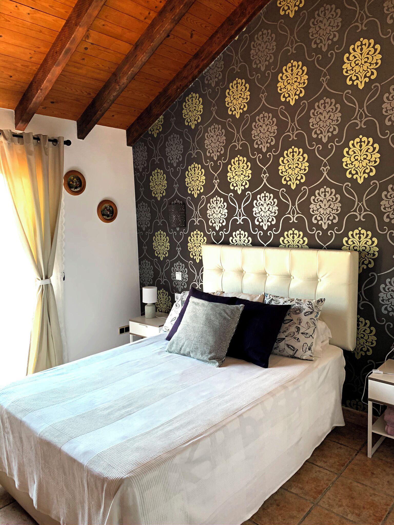 Une chambre à coucher avec un grand lit, un plafond en bois et un papier peint à motifs.