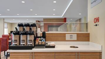 Una estación de café moderna con varios dispensadores, un cesto de basura y un cartel que dice 'Recreo Matutino'.