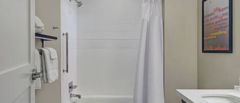 A bathroom with a bathtub, toilet, and a shower curtain. There are towels hanging on the wall and a sink with a mirror.