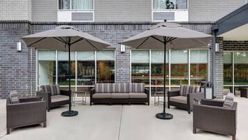An outdoor seating area with wicker furniture and umbrellas, a brick wall, and large windows.