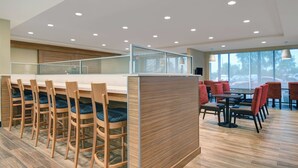 A modern restaurant with wooden chairs and tables, a high ceiling with recessed lighting, and large windows offering a view of the outdoors. - TownePlace Suites by Marriott Lima (Lima)