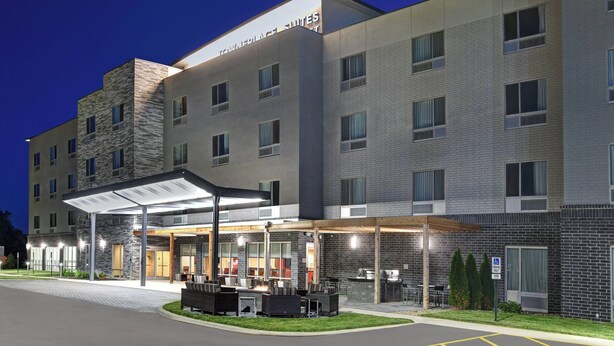 A hotel with a covered outdoor seating area, multiple windows, and a sign indicating a parking area. - TownePlace Suites by Marriott Lima (Lima)
