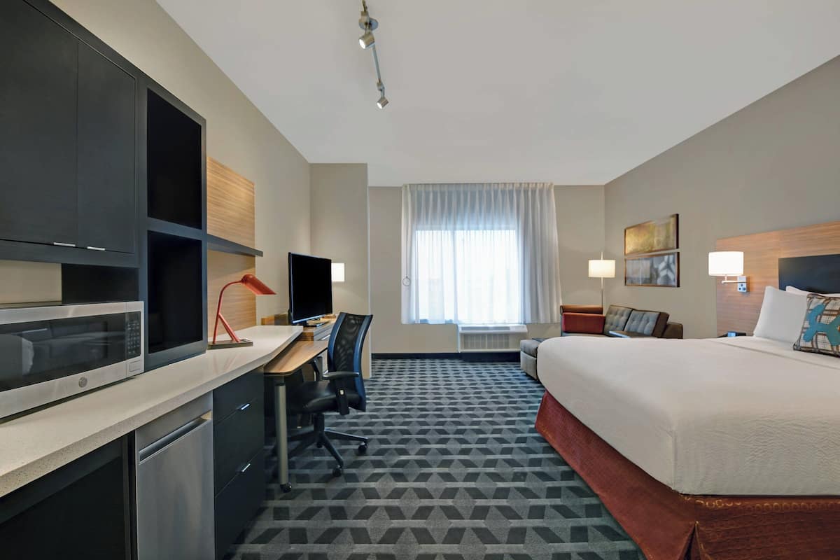 Una habitación de hotel con cama, escritorio, microondas y un amplio ventanal con cortinas.
