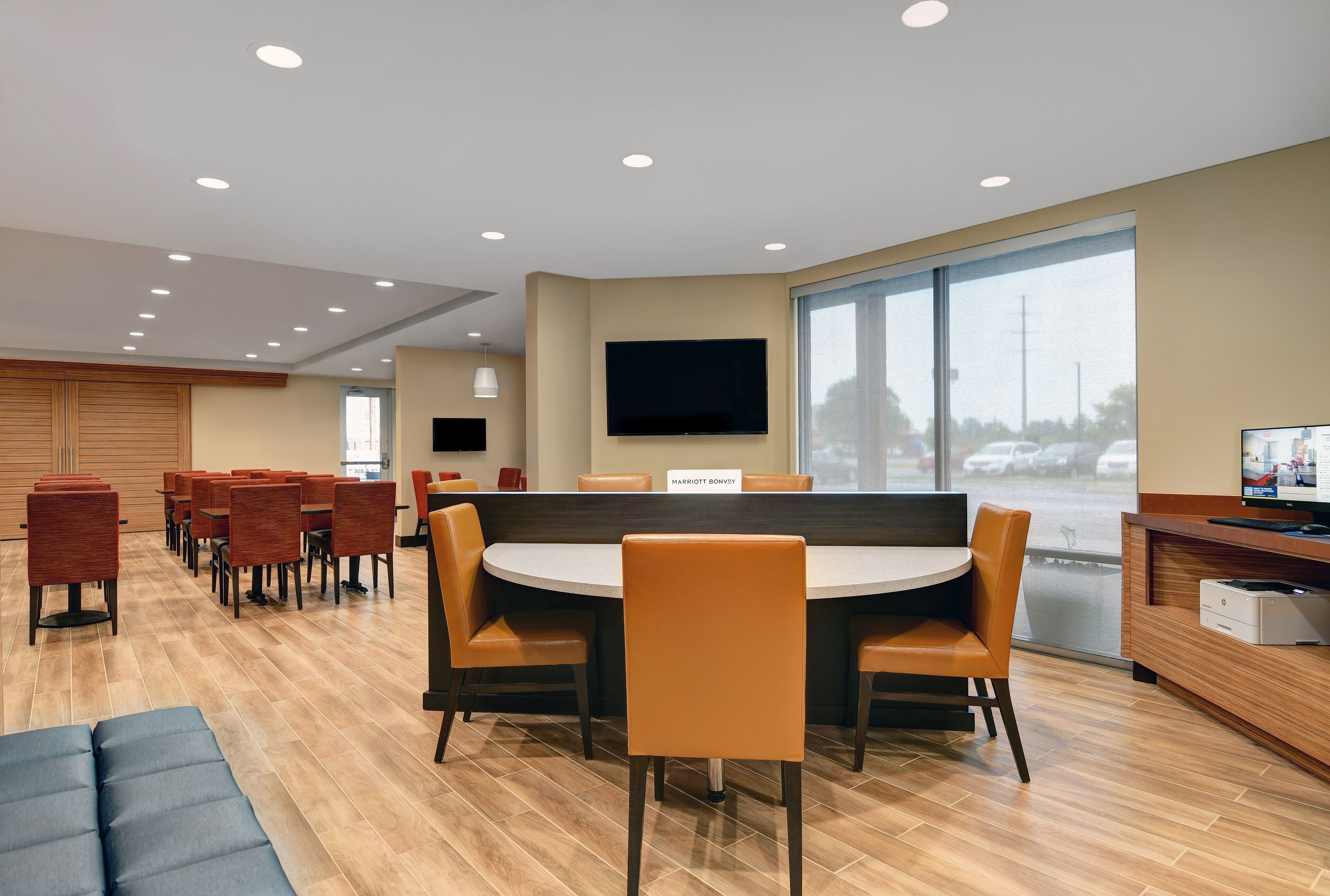 Um hall de hotel moderno com uma mesa redonda e cadeiras, uma televisão de tela plana e uma janela grande com vista para o exterior.
