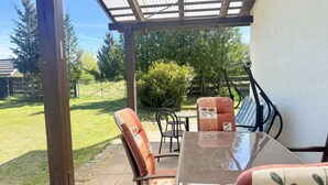 Patio esterno con tavolo e sedie, una pergola sopra e vista sul giardino circostante.