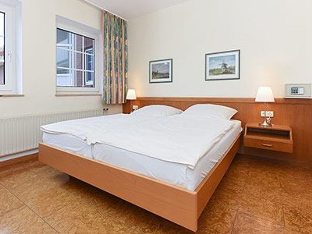 Een hotelkamer met een houten bed, twee nachtkastjes, een raam met gordijnen en twee ingelijste foto's aan de muur.