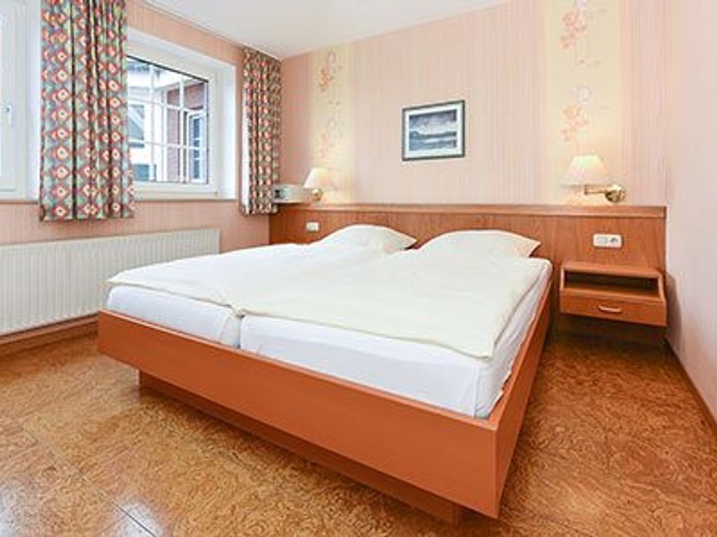 A bedroom with a wooden bed, a nightstand, a lamp, and a window with curtains.