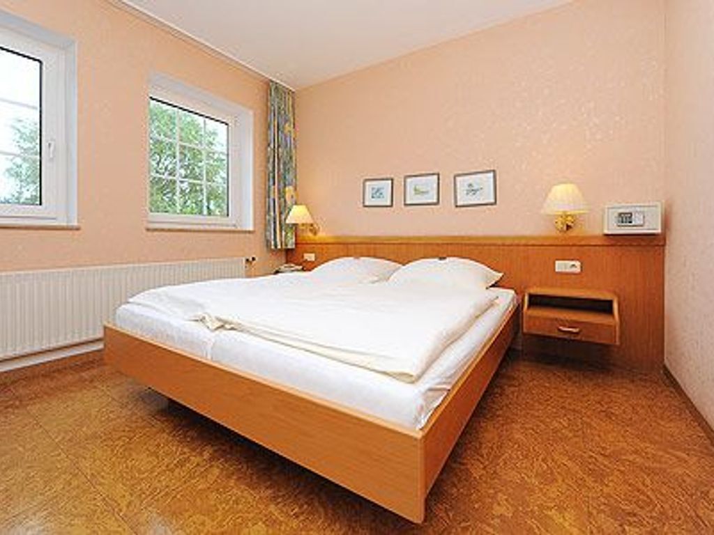 A bedroom with a wooden bed, a nightstand with a lamp, and a window with curtains.