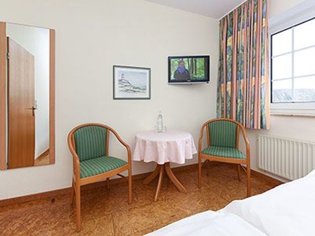 A hotel room with a bed, two green-striped chairs, a small round table, a television, a framed picture, and a window with curtains.