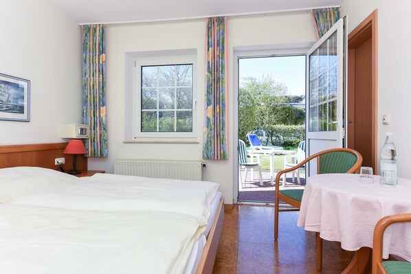 Une chambre d’hôtel avec un lit, une table recouverte d’une nappe, une chaise, une fenêtre et une vue sur l’extérieur.