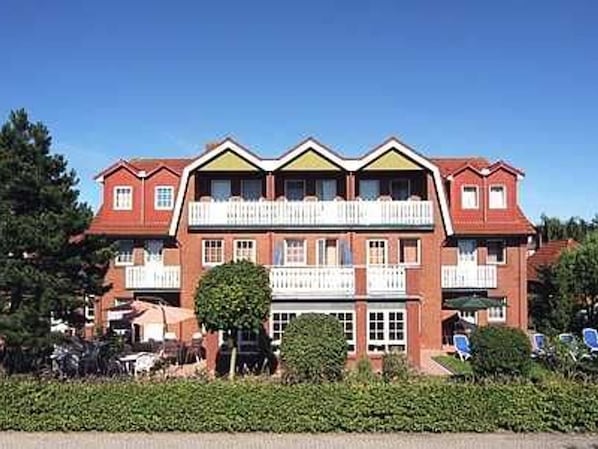 A multi-story hotel with a symmetrical facade, balconies, and a well-maintained garden area.