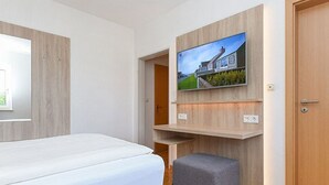 Ein Hotelzimmer mit einem Bett, einem an einer Holzplatte montierten Fernseher, einem kleinen Schreibtisch und einer Tür.