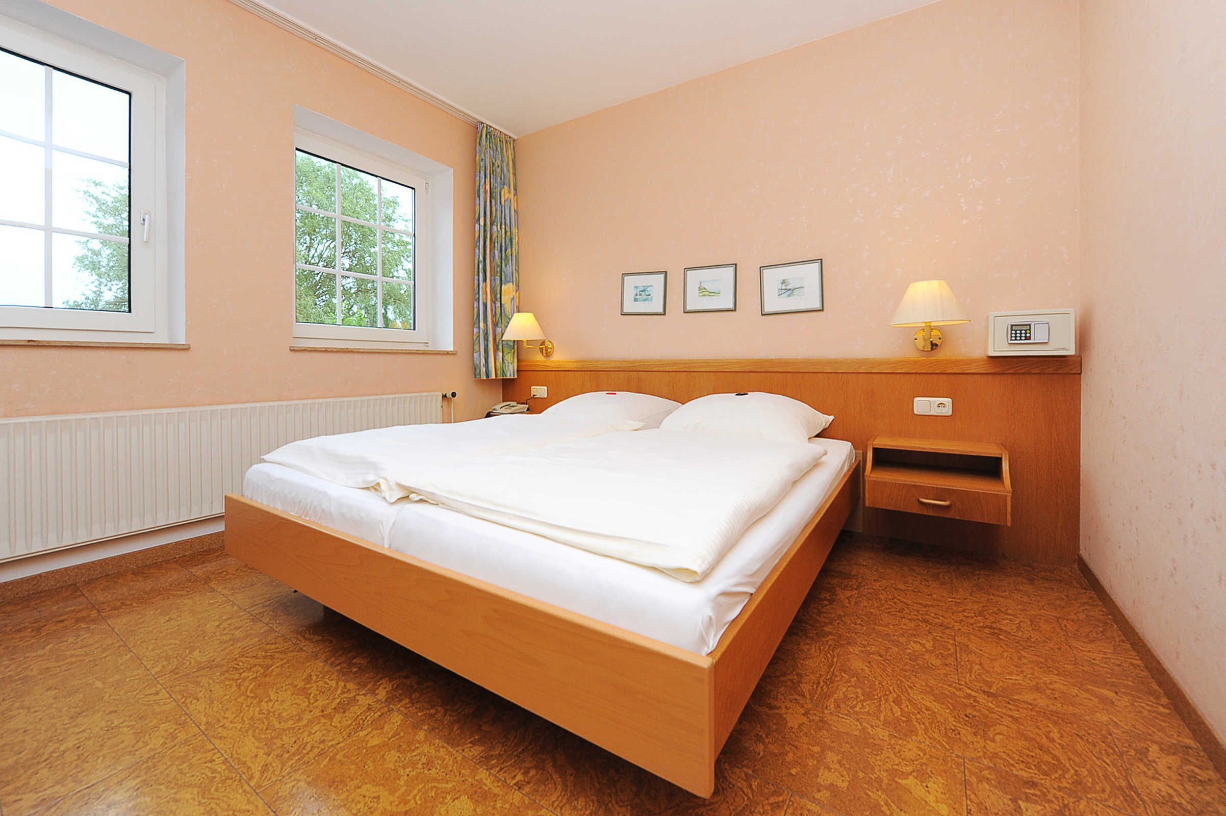 A hotel room with a wooden bed, a nightstand, a lamp, and a window with a view of trees.