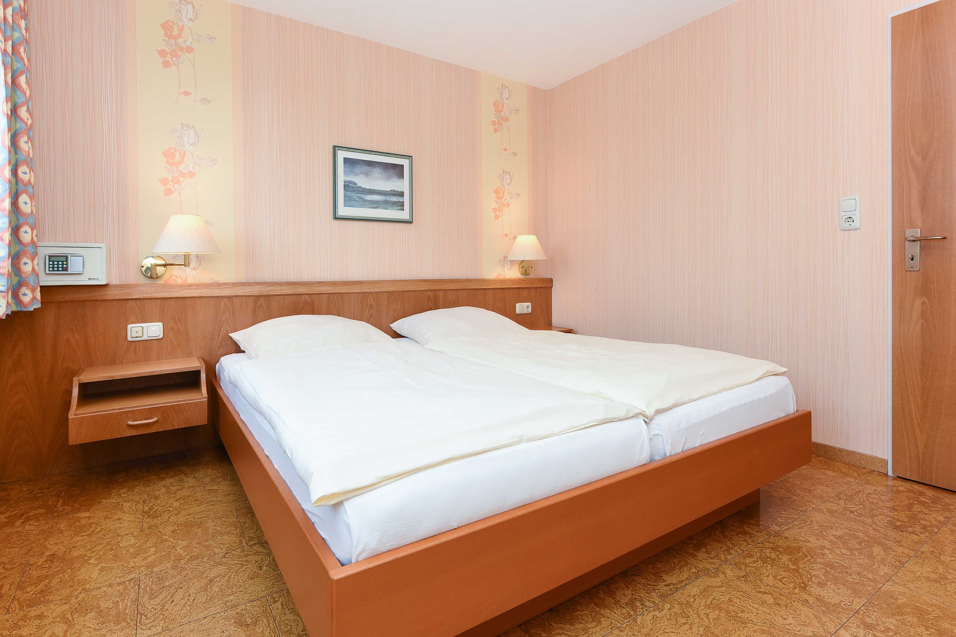 Une chambre à coucher avec un lit en bois, deux tables de chevet avec des lampes, une petite table et une prise de courant fixée au mur.
