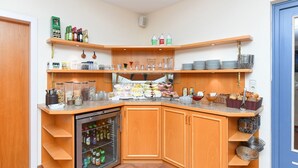A corner kitchen area with a refrigerator, shelves with bottles, and various kitchenware. - Double room non-smoking category I - Double room in the Hotel-Pension (Esens)
