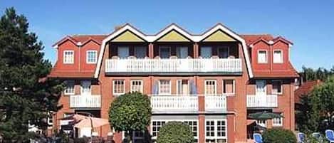 A multi-story hotel with a symmetrical facade, balconies, and a well-maintained garden area.