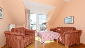 Ein gemütliches Wohnzimmer mit gestreiftem Sofa, einem Tisch mit Tischdecke und einem Fenster mit Vorhängen.