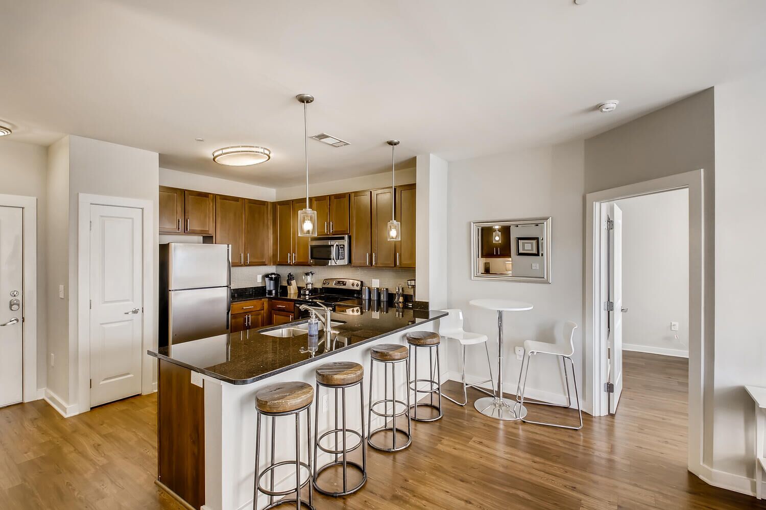 Una cocina moderna con armarios de madera, electrodomésticos de acero inoxidable, una isla central con taburetes e iluminación colgante.