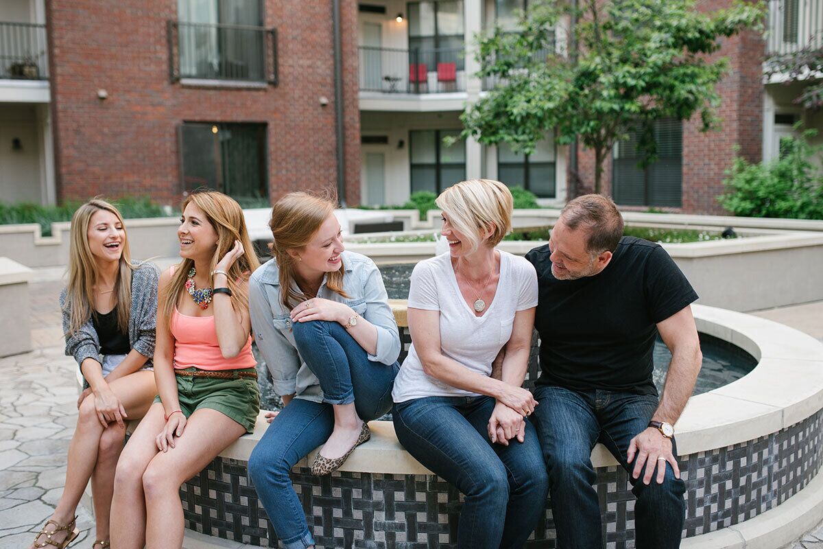 A group of people sitting on a circular bench in an outdoor courtyard with a brick building in the background.