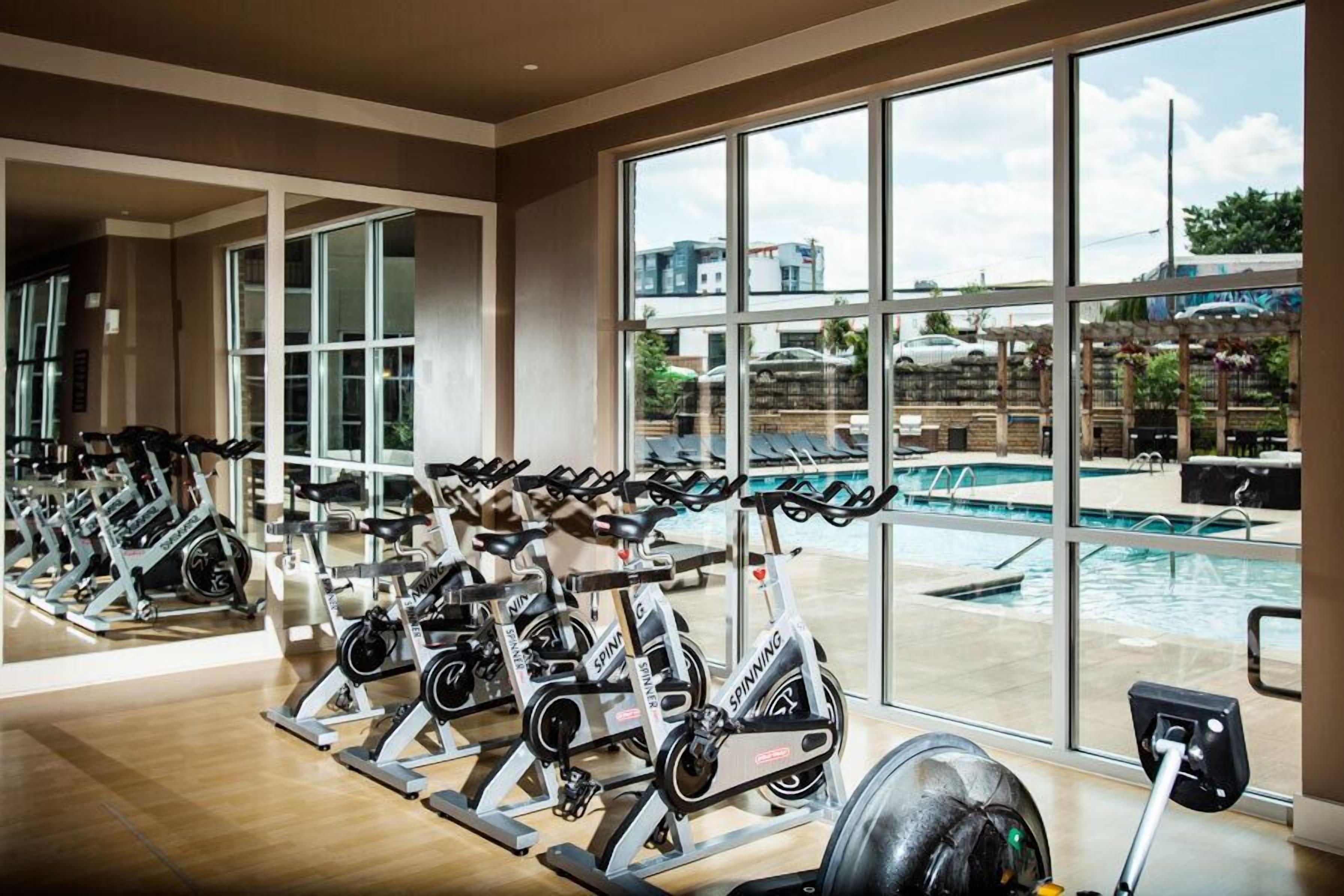 A gym with stationary bikes and a view of a swimming pool through large windows.