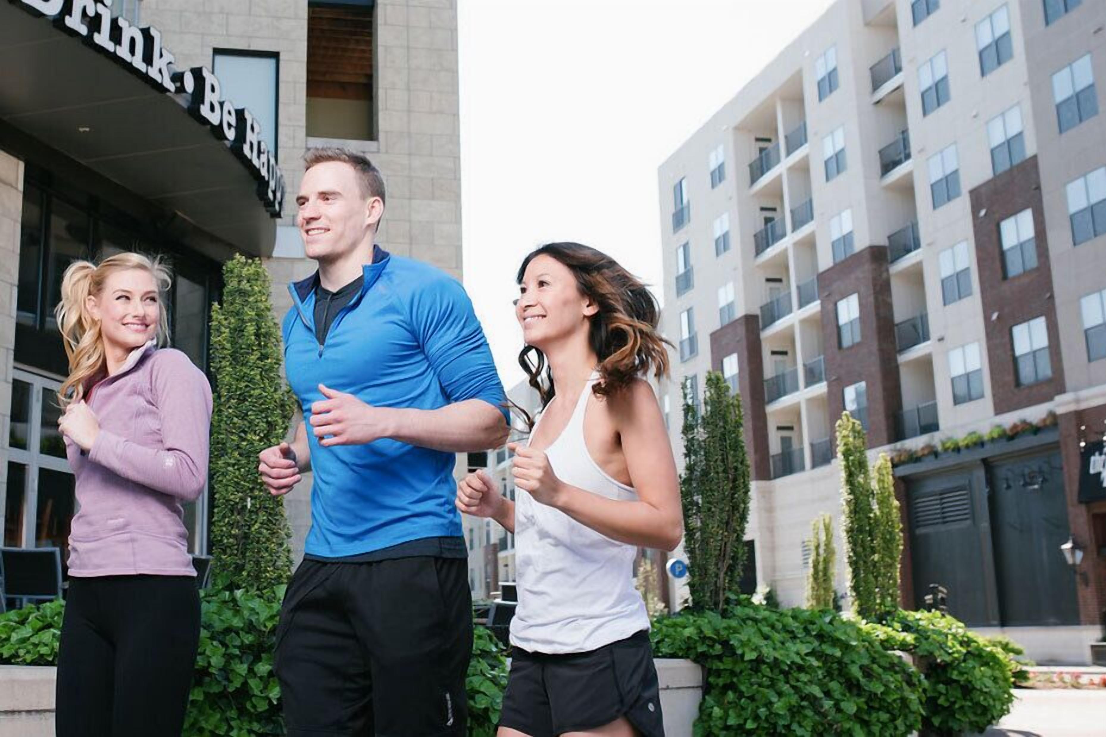 Three people jogging in front of a building with a sign that reads "Drink. Be Happy."