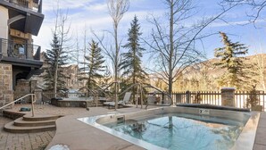 A swimming pool with steps leading into it, surrounded by trees and a stone building. - Incredible Snowmass Condo by Gondola! Walk to Dining & Shops. A/C, Hot Tubs, Balcony, W/D, Parking! (Snowmass Village)